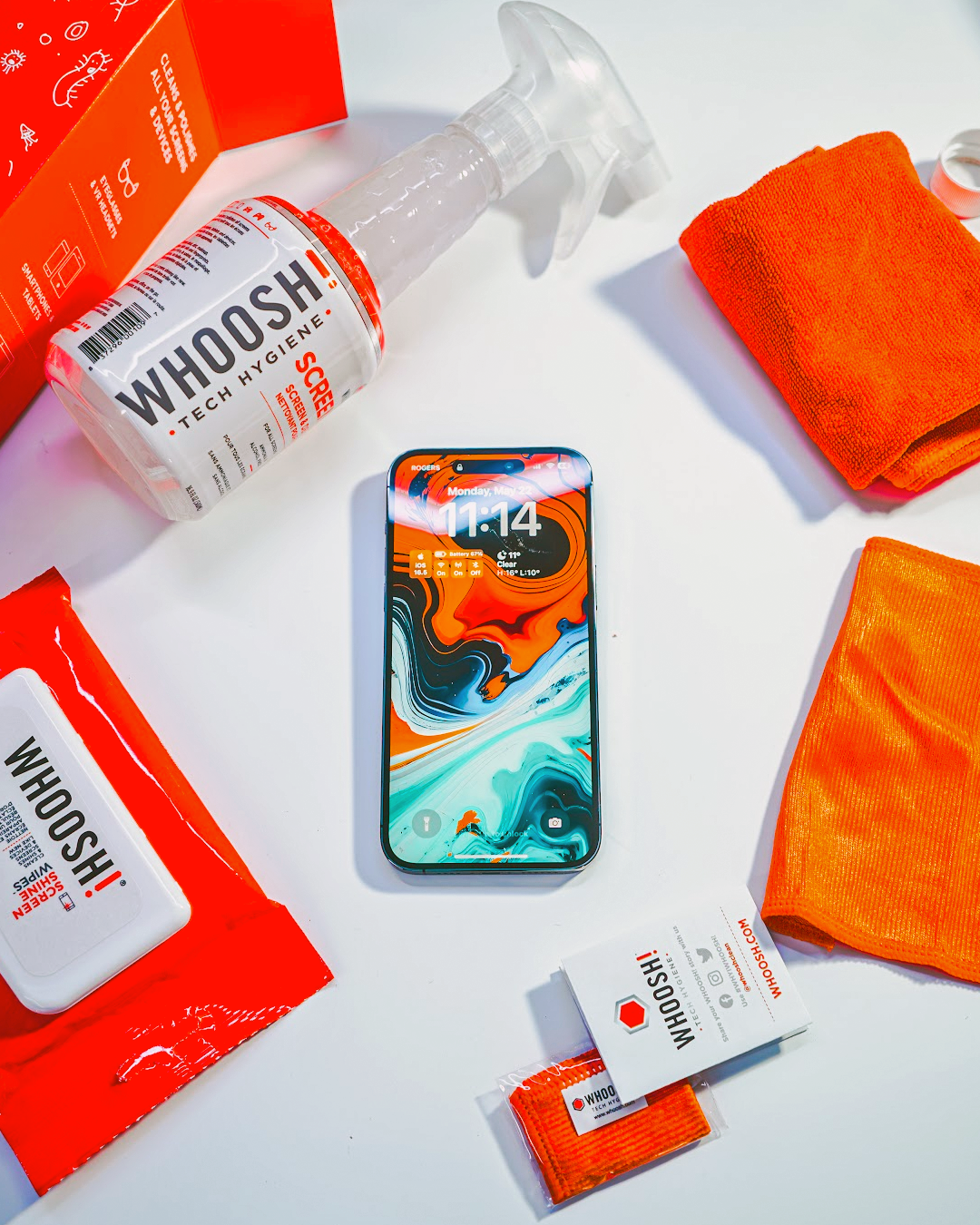 Smartphone surrounded by WHOOSH! screen cleaner, wipes and orange microfibre cloths, showing an easy, safe way to keep phone screens clean, clear and fingerprint-free.
