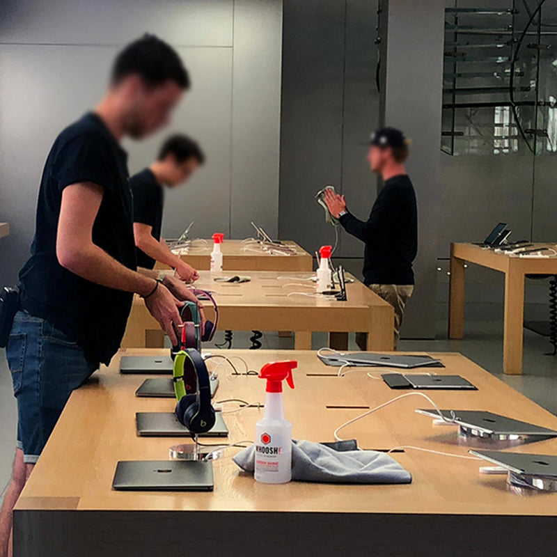 Retail staff cleaning laptops, tablets and headphones with WHOOSH! screen cleaner, keeping shared devices hygienic and fingerprint-free in a busy tech store.